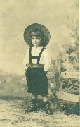 Enfant debout lavec chapeau de paille les mains dans les poches devant une barrière